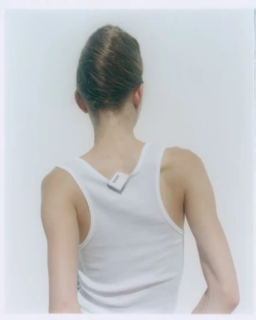 Back view of a young adult female with updo wearing a white tank top; a small sensor device is attached to the upper back.