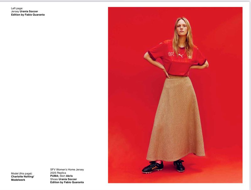 Fashion editorial shot of a woman in a red jersey and tan skirt against a solid red backdrop. The image is well-lit and composed.