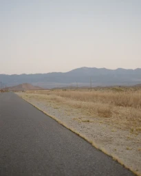 An open asphalt road cutting diagonally through dry desert grasslands toward distant blue mountains under a pale sky.