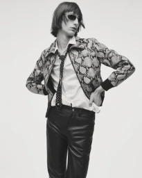 Model wearing a patterned snakeskin-print jacket, polka-dot tie, and dark pants against a plain background.
