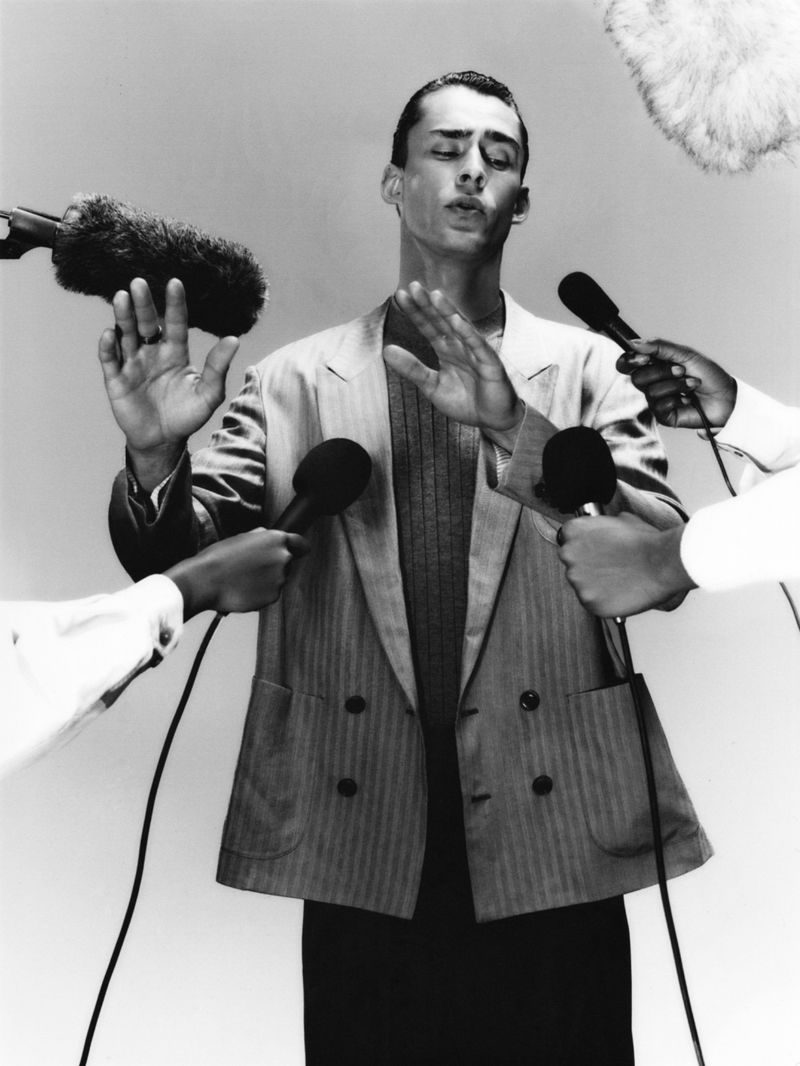 Model Ange-Marie Moutambou raising hands in front of microphones wearing a striped double-breasted blazer in black and white.