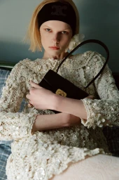 Model in textured cream dress holding black handbag wearing headband
