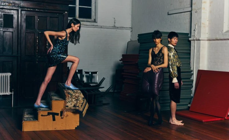 Three fashion models posing in an industrial interior with dark wood and stacked green mats, photographed by Angelo Dominic Sesto for ODDA Magazine