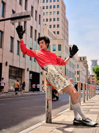 Model posing dynamically against a street bollard wearing a red cropped sweatshirt, patterned shorts, and black gloves.