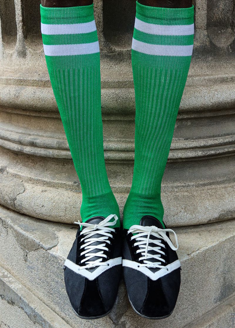 Close-up of a person's legs wearing bright green knee-high tube socks with white stripes and black low-profile lace-up sneakers.