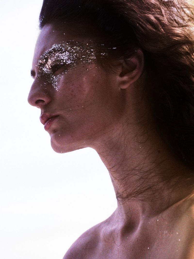 Close-up profile of a model with silver glitter makeup around the eye against a bright white background.