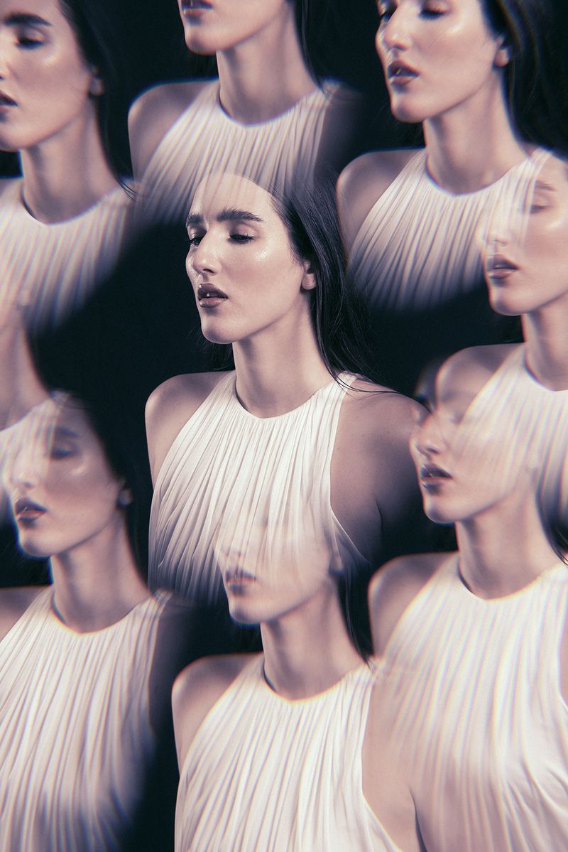 Woman with long hair poses in halter top with multiple exposure effect in front of a black background with soft, diffused lighting.
