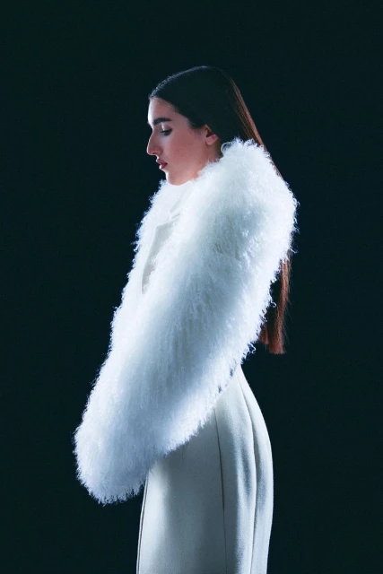 Elegant portrait of a woman in profile wearing a white coat with a fur collar against a black background in a studio setting.