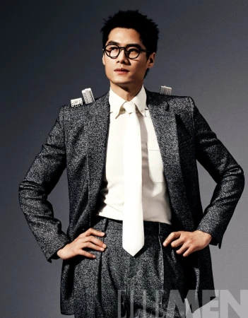 Portrait of Asian man in a grey suit and tie, posing with hands on hips, wearing black glasses, with miniature building props on shoulders.