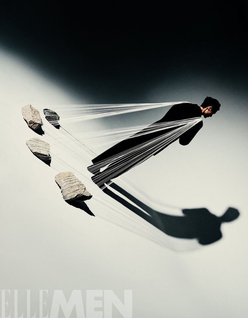 Fashion shot of a man in black suit jacket tethered to levitating stones, artistic composition, studio lighting, and modern style elements.