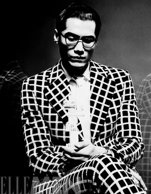 Man wearing a black and white grid patterned suit and glasses holding a building model in a monochrome portrait