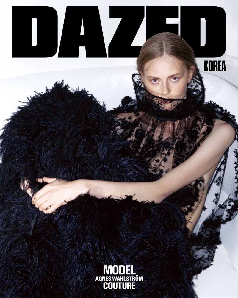 Model Agnes Wahlström in a voluminous black feathered dress with a lace collar inside a white bathtub for Dazed Korea.