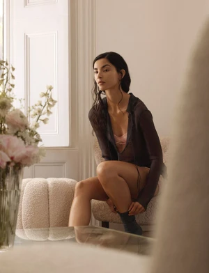 Model Tindi Mar sitting in a textured chair indoors wearing a dark sheer top for Vogue Thailand, captured by photographer Amie Milne.