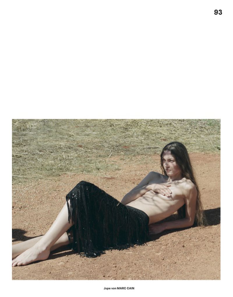Model lying on reddish dirt ground wearing a black fringe skirt outdoors in Annabelle Magazine editorial