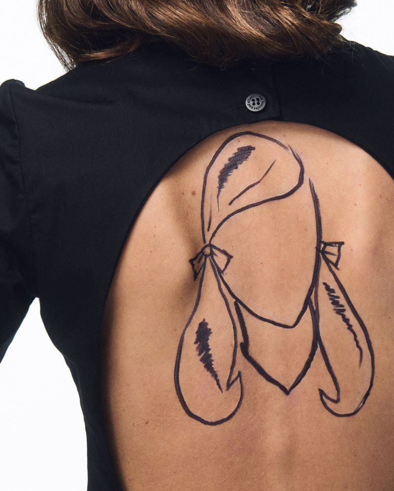 Back view of a person wearing a black dress with a cartoon woman's face drawn on their back in a minimalistic style.