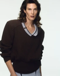 A female model wearing a dark brown ribbed knit sweater against a plain white studio background.