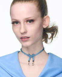 Close-up portrait of a woman wearing a blue top and a blue ribbon choker necklace against a white background