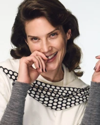 Portrait of a smiling woman with dark hair wearing a white top and polka dot scarf against a white background