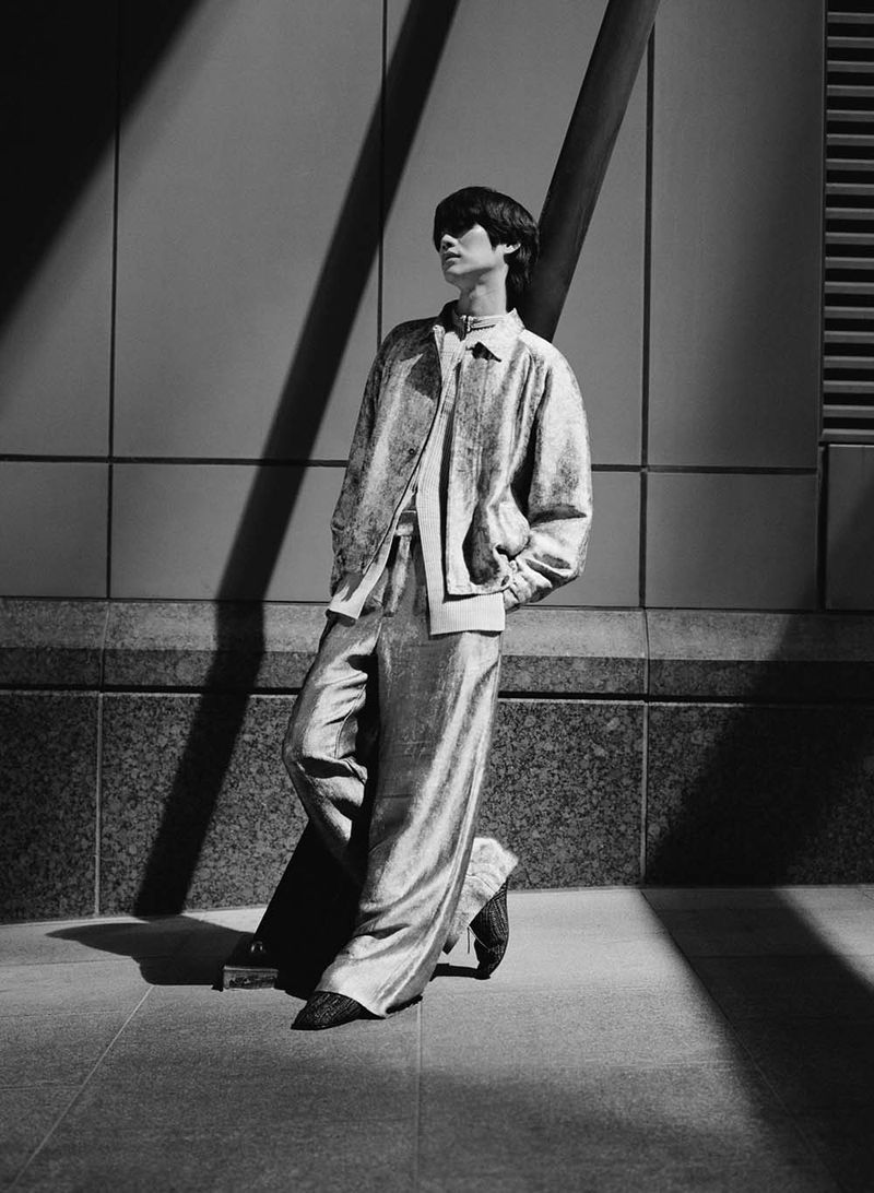 Black and white portrait of Sanggun Lee leaning against an exterior wall with diagonal shadows.