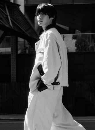 Black and white portrait of model Sanggun Lee wearing an oversized light jacket and matching wide trousers in an urban street setting.