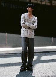 Model Sanggun Lee standing on a paved street wearing a patterned beige v-neck sweater and wide-leg dark grey trousers.