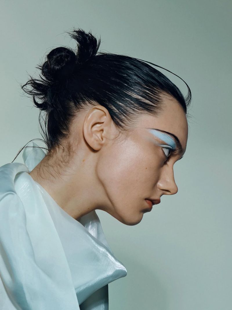 Woman in profile with creative makeup and a white garment, soft lighting, and smooth skin, captured in a beauty or fashion editorial.