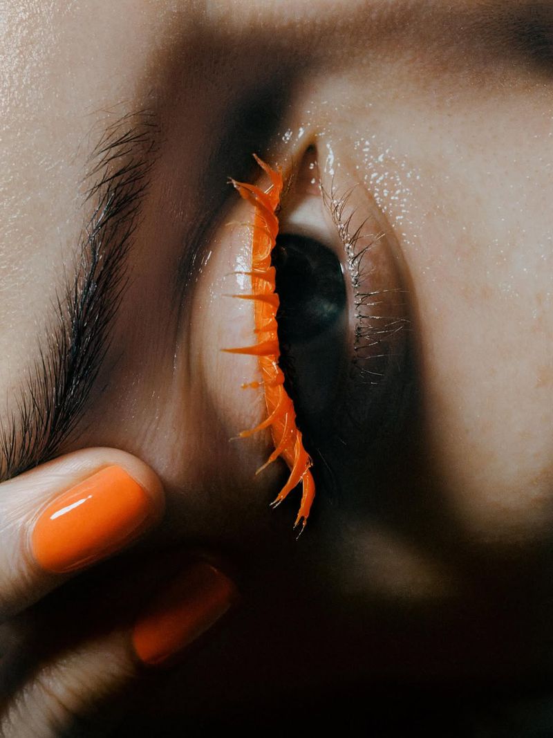 Macro shot of a human eye adorned with vibrant orange, spikey, organic-like fringe, accentuating the eyelashes and skin details.