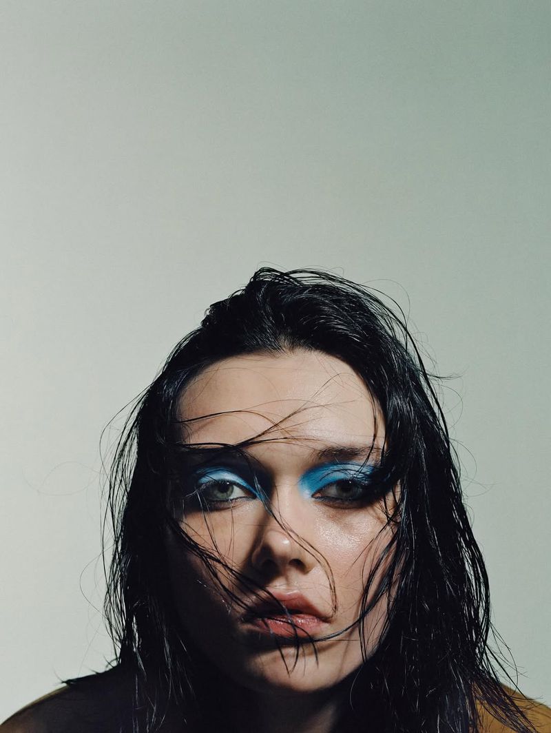 Close-up portrait of a woman with wet dark hair and vibrant blue eyeshadow against a plain background
