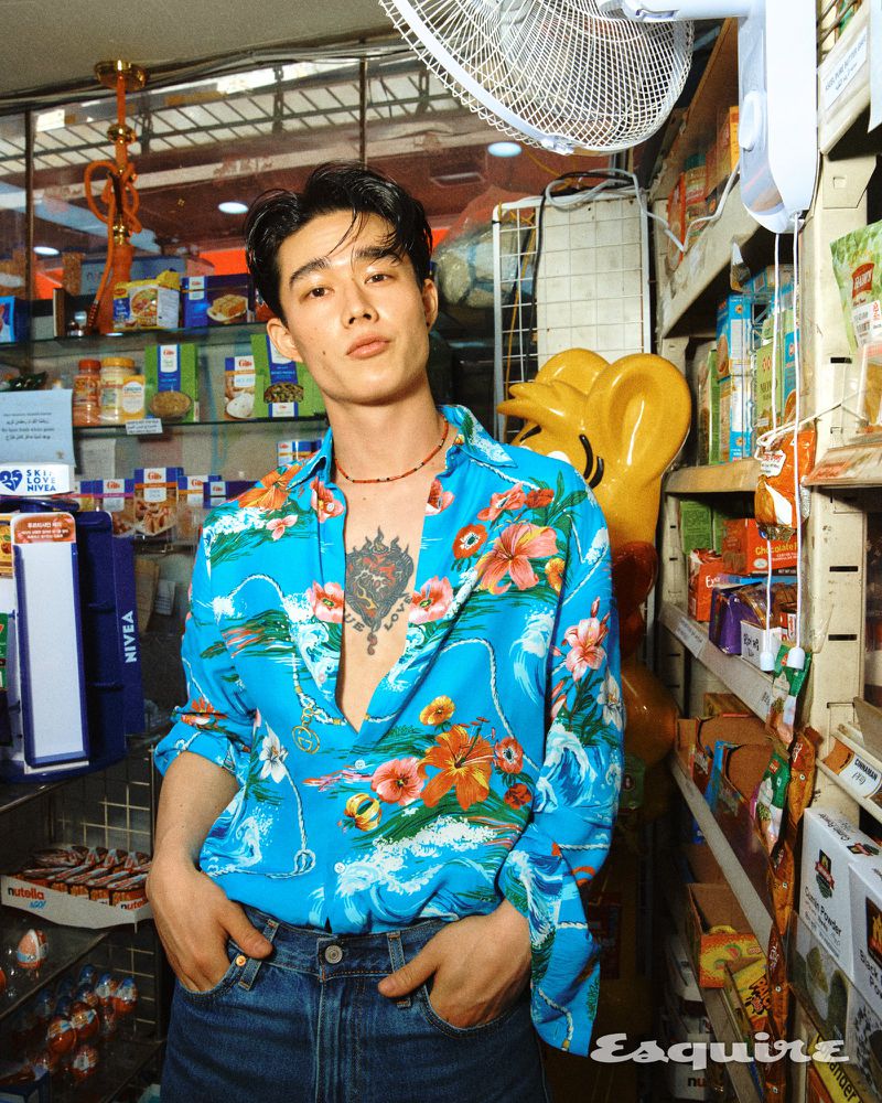 Joji Iwase poses in an open bright blue floral shirt and denim jeans inside a convenience store for Esquire Korea.