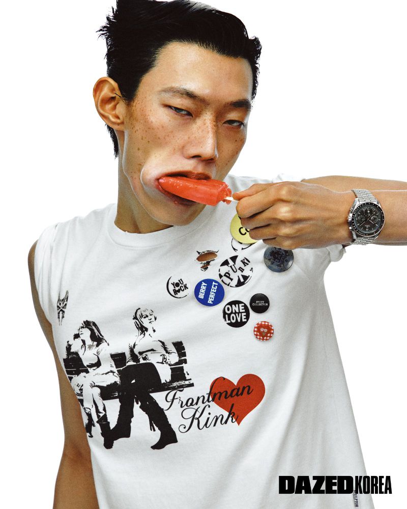 Hoyong Kim eating an orange popsicle in a white graphic tank top with pin badges for Dazed & Confused Korea.