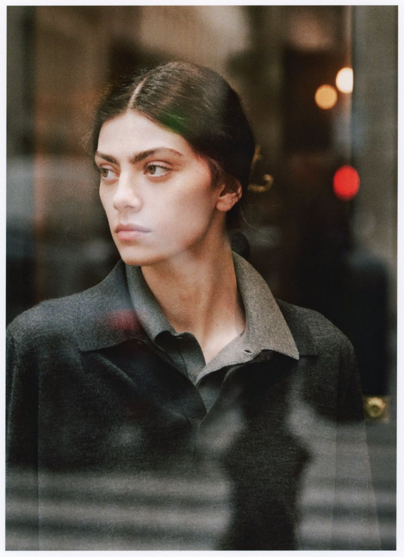 Portrait of a woman with dark hair and grey collared shirt looking to the side in an indoor environment with natural lighting.