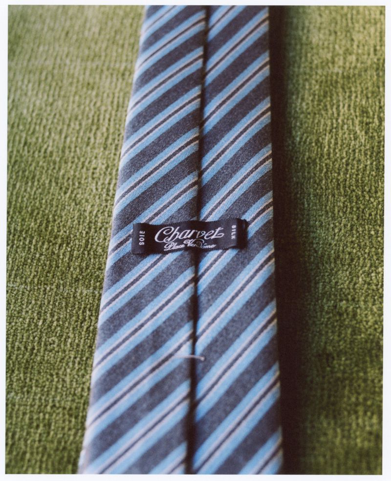 Close-up of a striped blue and gray Charvet silk tie on textured green fabric, showcasing elegance and refined menswear accessory.