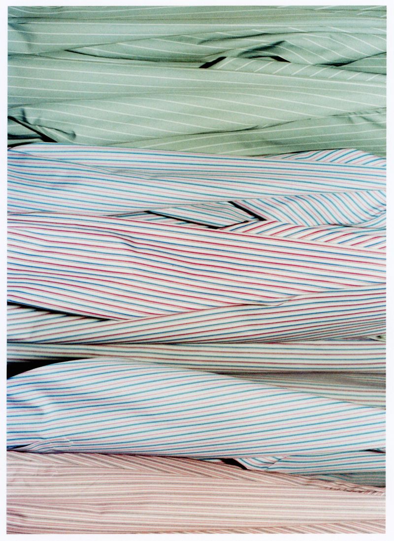 Stacked layers of striped cotton fabrics in pastel shades of green, blue, red, and pink, creating a soft, textured background.