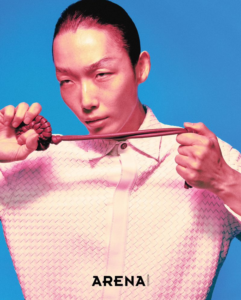 Model Xu Meen holding a braided leather cord in front of a woven white button-up shirt against a vivid blue background.