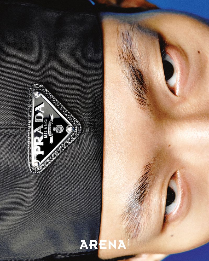 Extreme close-up portrait of an East Asian man wearing a black nylon Prada cap with a triangular logo plaque.