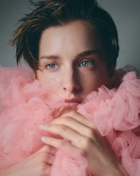 Close-up portrait of a model with short dark hair surrounded by voluminous pink tulle fabric