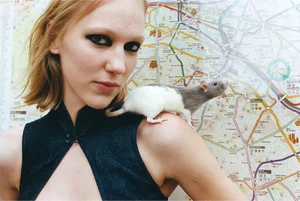 Model with dark eye makeup posing in front of a transit map with a small rat on her shoulder for Unprint Magazine