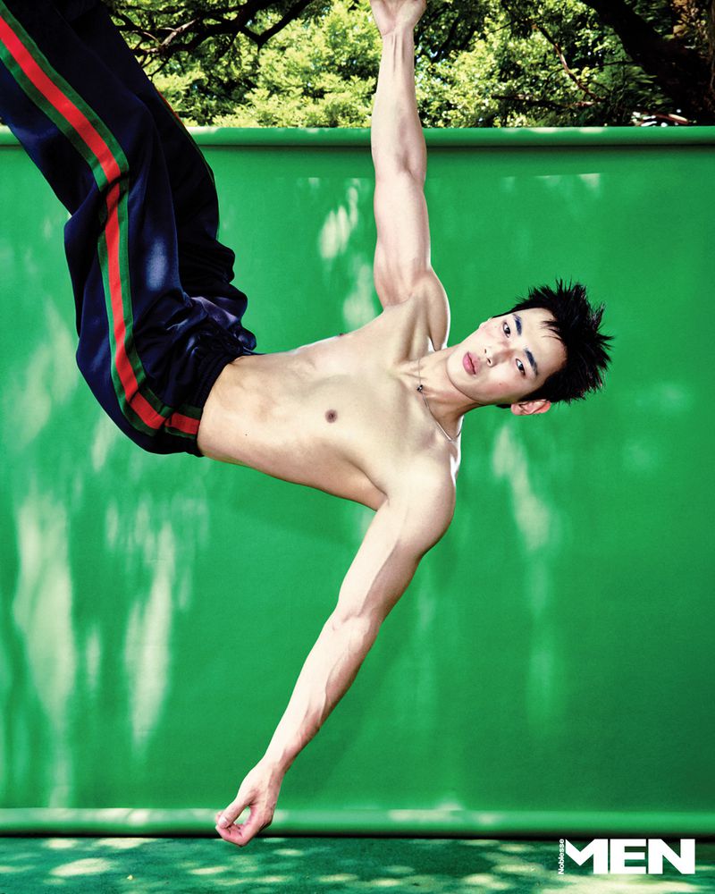 Shirtless male model hanging from an overhead bar against a vibrant green studio backdrop for Noblesse Korea Muscle Memory project.