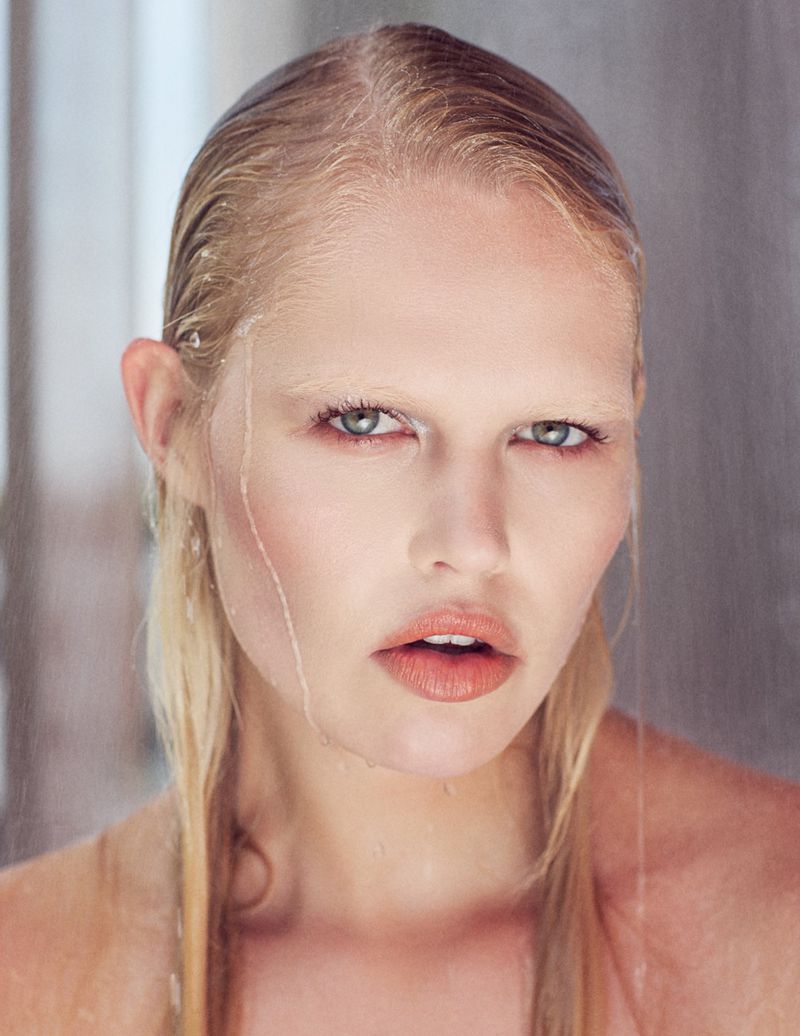 Close-up beauty portrait of a blonde woman with wet hair, bleached eyebrows, and water dripping down her face against a soft background.