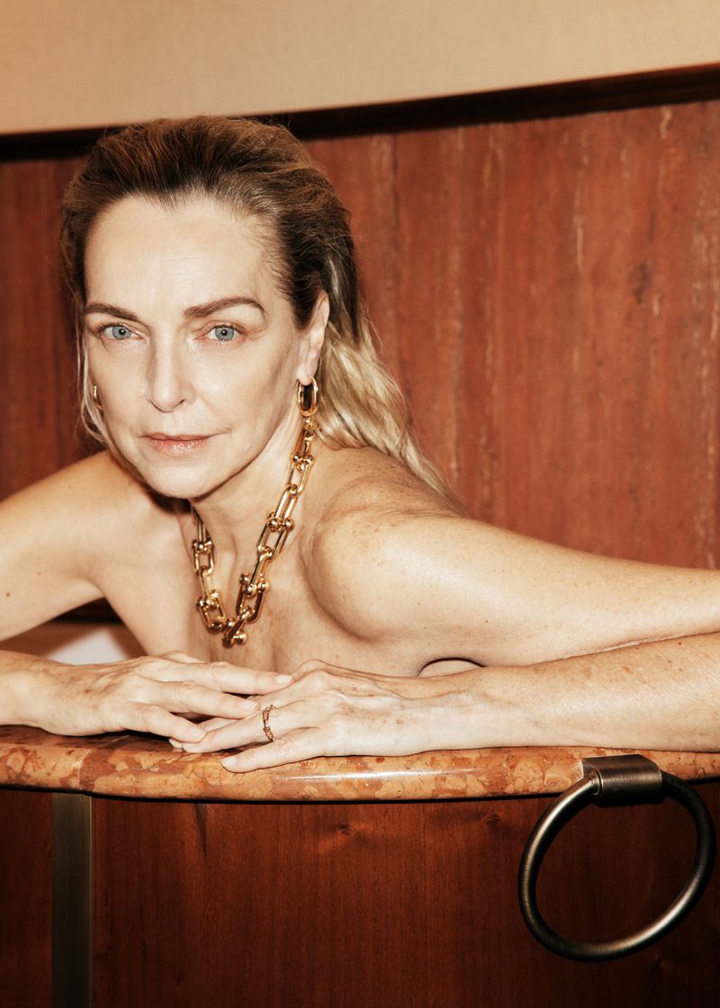 Model Simonetta Gianfelici resting her arms on the edge of a wooden bathtub wearing a chunky gold chain necklace.
