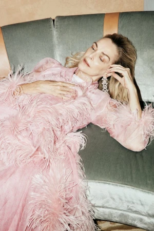 Model Simonetta Gianfelici reclining on a velvet sofa wearing a voluminous light pink feather-trimmed dress and statement earring.