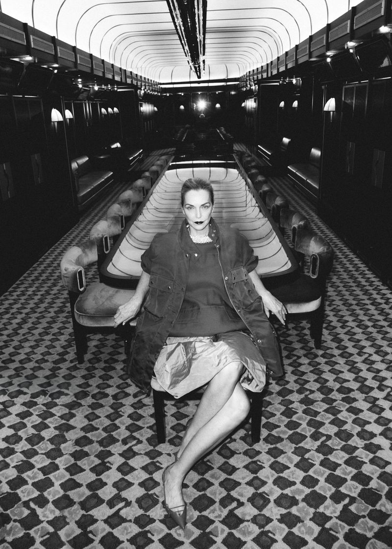 Model Simonetta Gianfelici seated in an opulent train carriage wearing a sleeveless utility jacket, full skirt, and pointed heels.