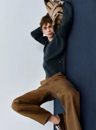 Model wearing a dark grey cardigan and brown trousers holding a bag in a fashion editorial for Numero Switzerland.