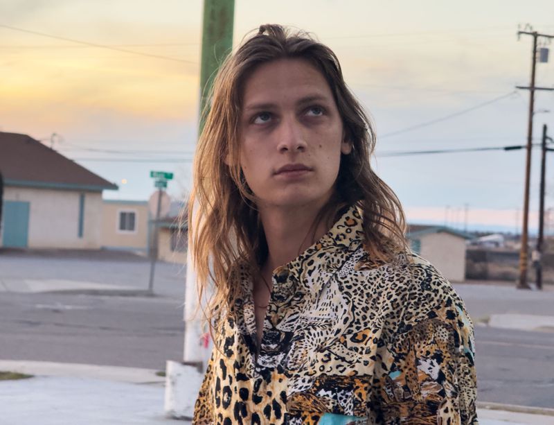 Model Jesse Rinderknecht wearing a leopard print collared shirt outdoors at dusk against a suburban street background.