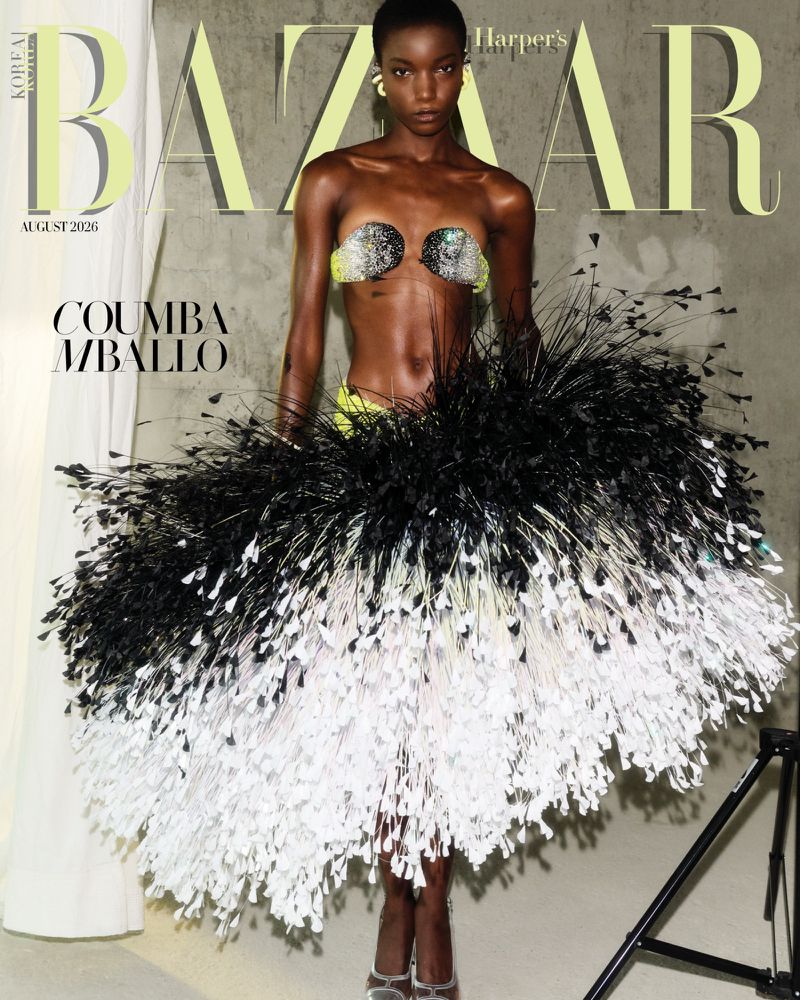 Model Coumba Mballo wearing a feathered skirt and beaded top against a textured grey background for a magazine cover