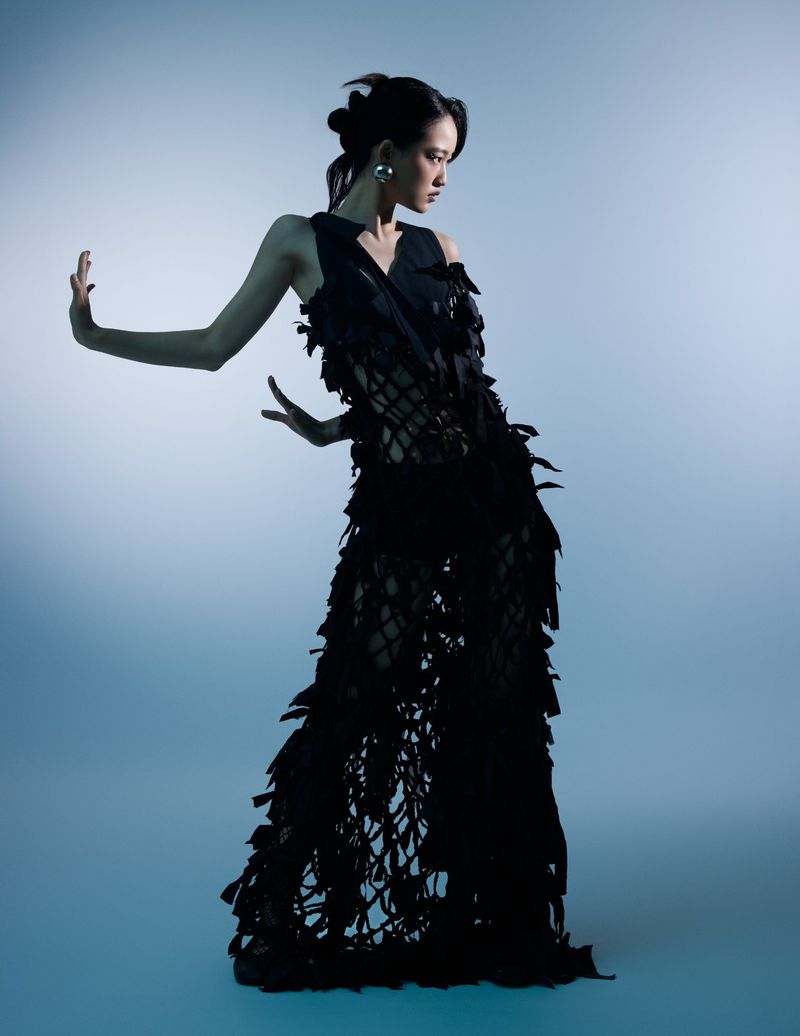 Model in a black textured fringe gown posing against a blue studio background