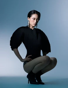 Model in dark sculptural top and high heels crouching against a blue studio background for L'Officiel Arabia