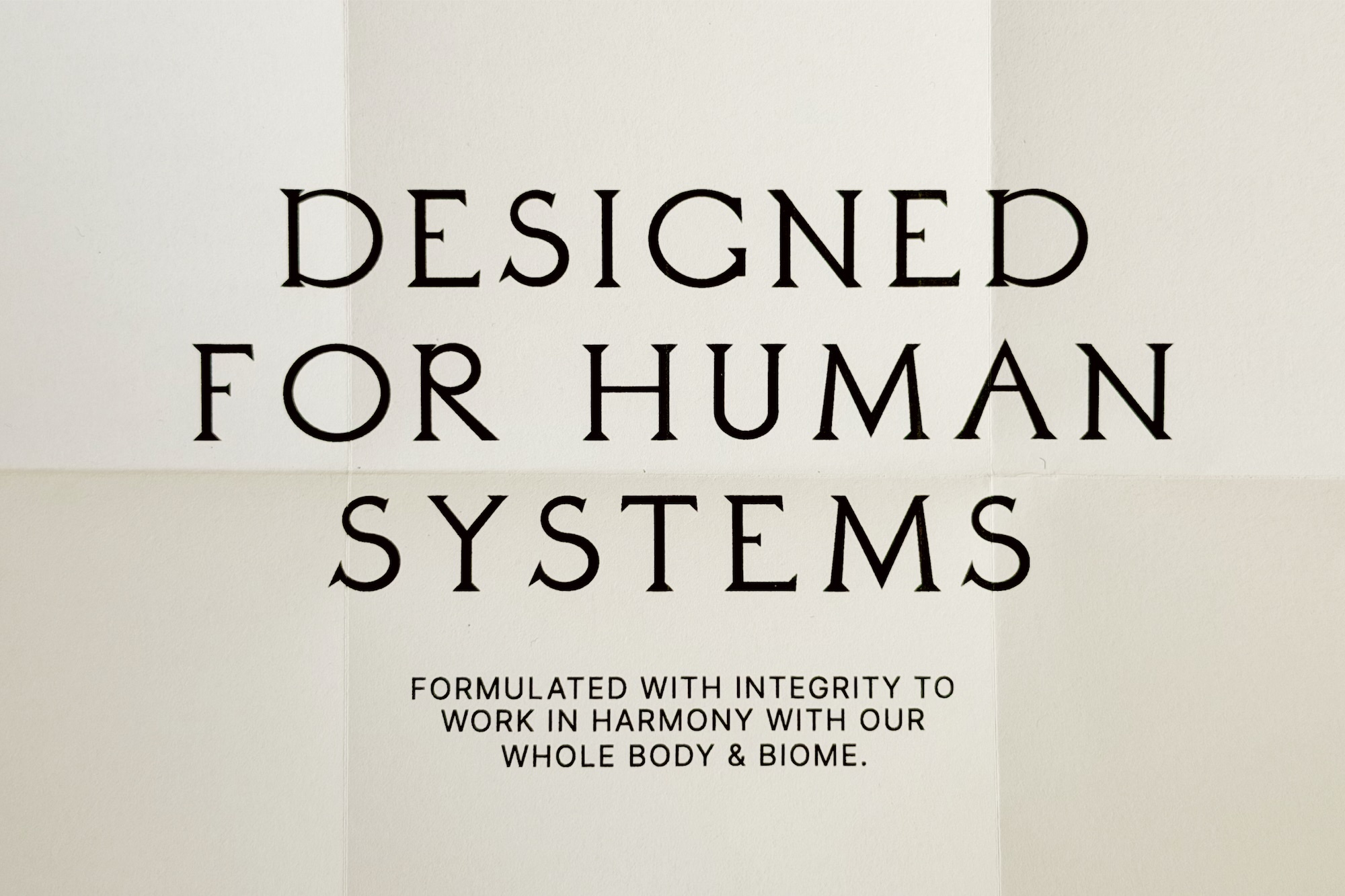 Black serif typography reading 'Designed For Human Systems' printed across a folded off-white paper panel.