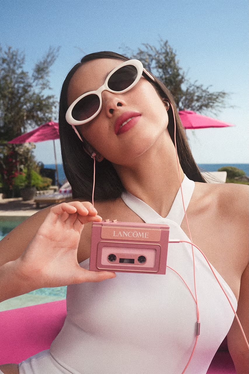 Olivia Rodrigo wearing white oval sunglasses and a halter top, holding a pink Lancôme cassette player poolside.