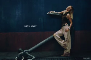 Bella Hadid posing against a large ship anchor in wide-leg distressed pants and a sleeveless top for Miss Sixty.